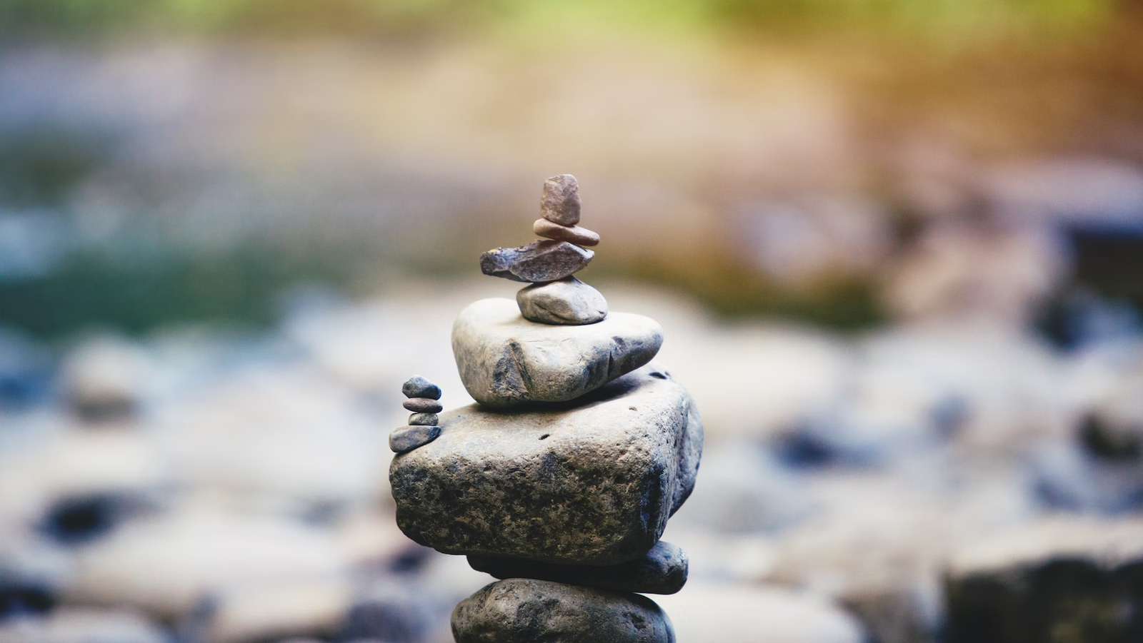 Stacked rocks near a river with blurry background, in the style of playful symbolism, for mindfulness and balance